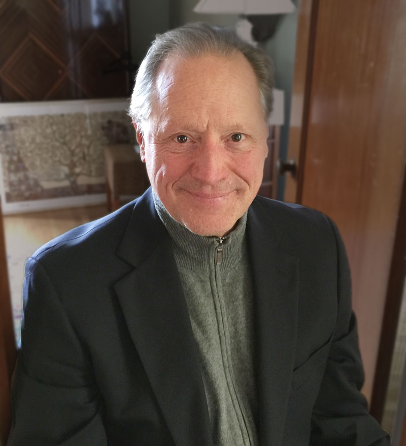 A man in a suit and jacket smiling for the camera.